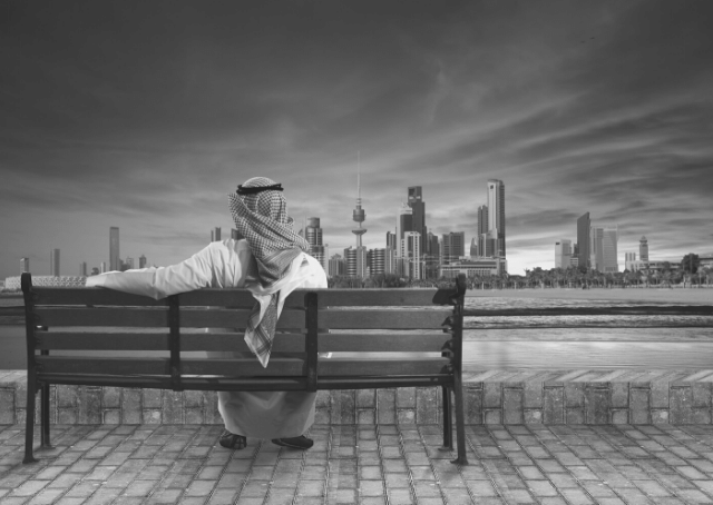 Uomo seduto su una panchina che guarda la città del Kuwait